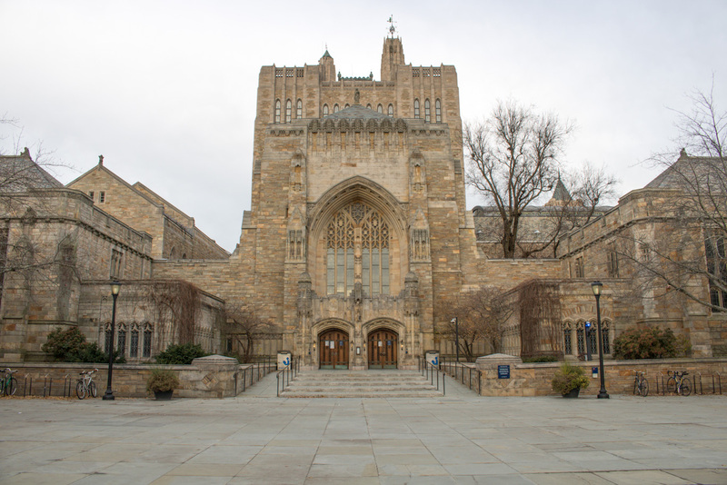 Sterling Memorial Library exterior, 2021; large, neo-Gothic gray stone building with two wood doors for entry